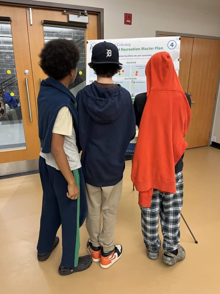 Three young people reading an engagement board, seen from behind